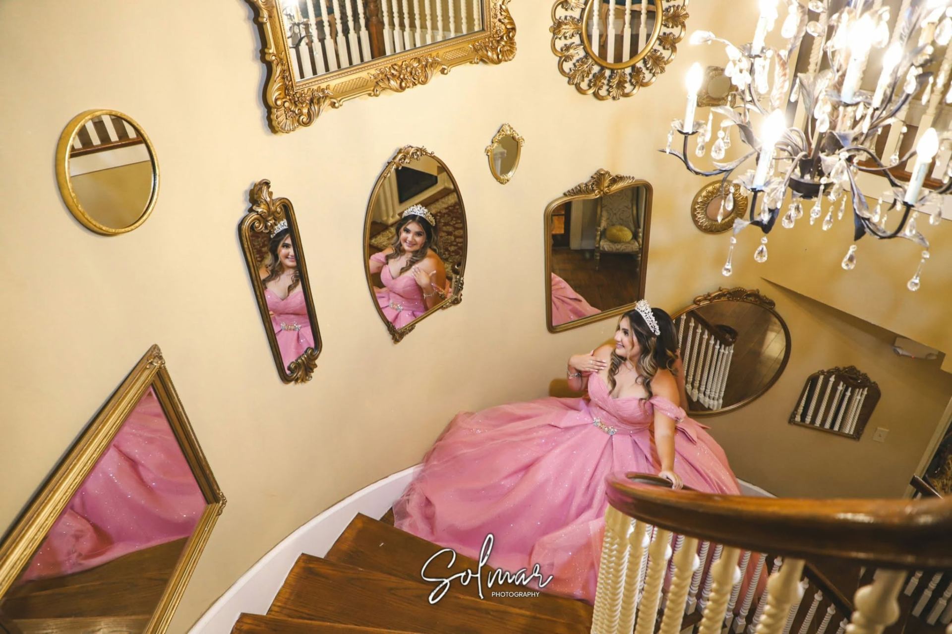 Quinceañera in pink gown on staircase surrounded by ornate gold mirrors