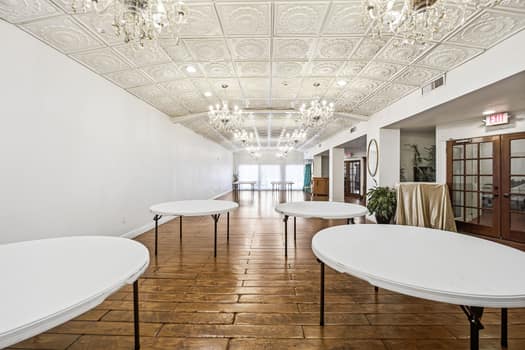 Small venue with white folding tables beneath chandeliers and a patterned ceiling