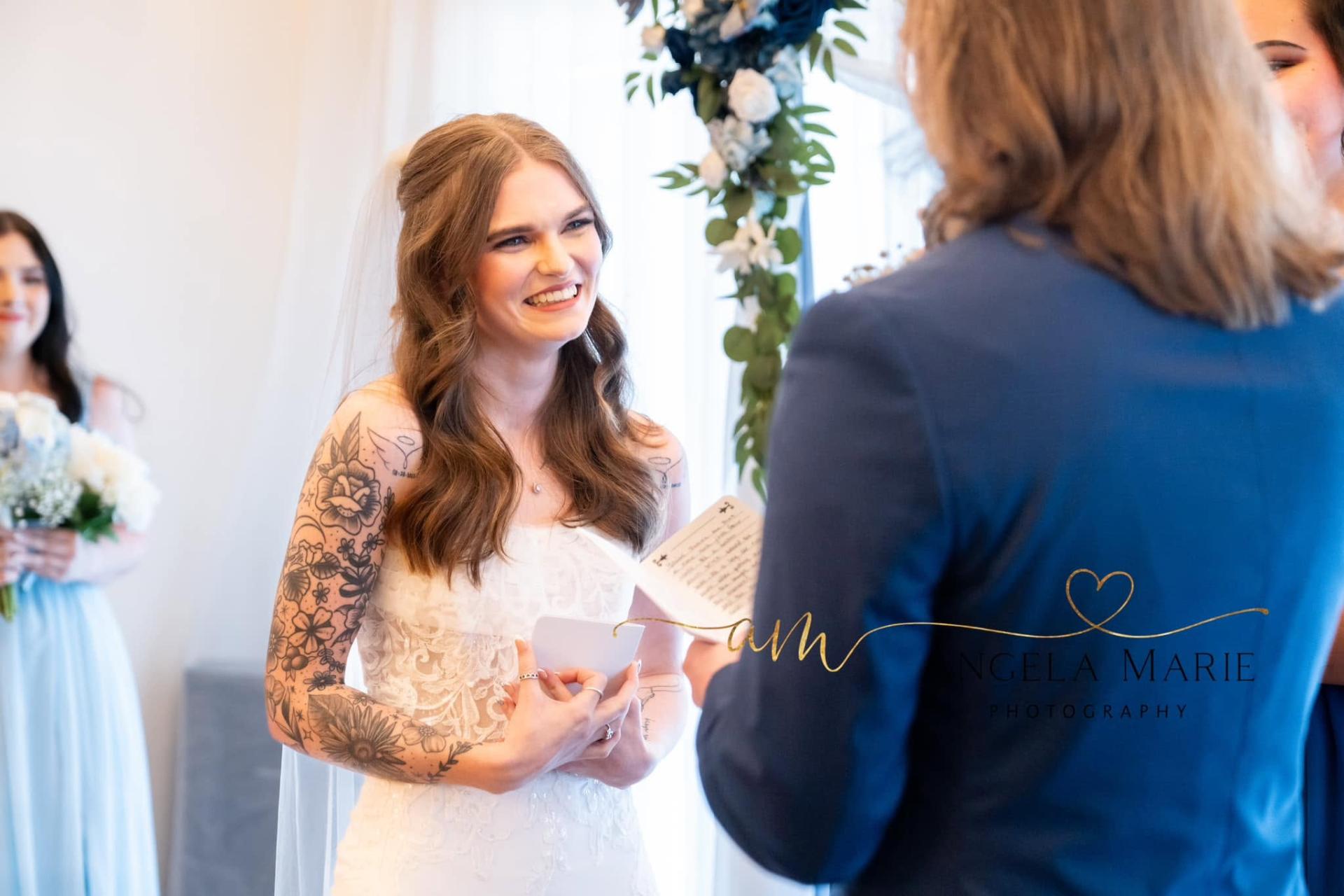 Bride smiling while exchanging vows beneath a floral arch
