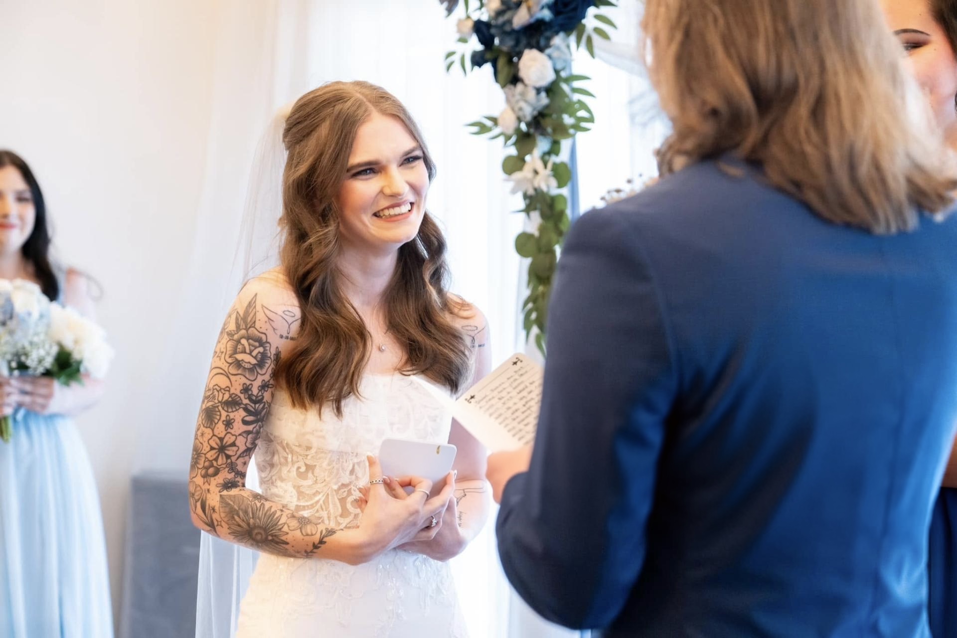 Bride smiling while exchanging vows beneath a floral arch