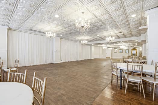 Grand venue dance floor framed by white drapery and crystal chandeliers