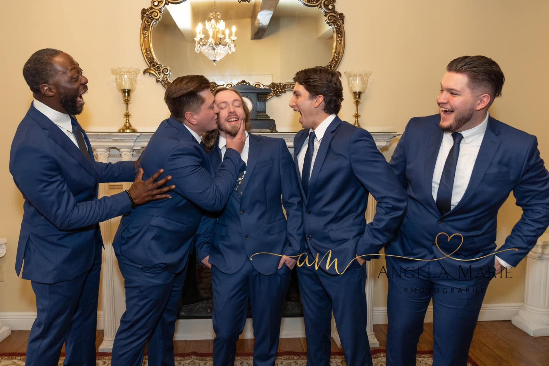 Groomsmen laughing together in navy suits by the fireplace