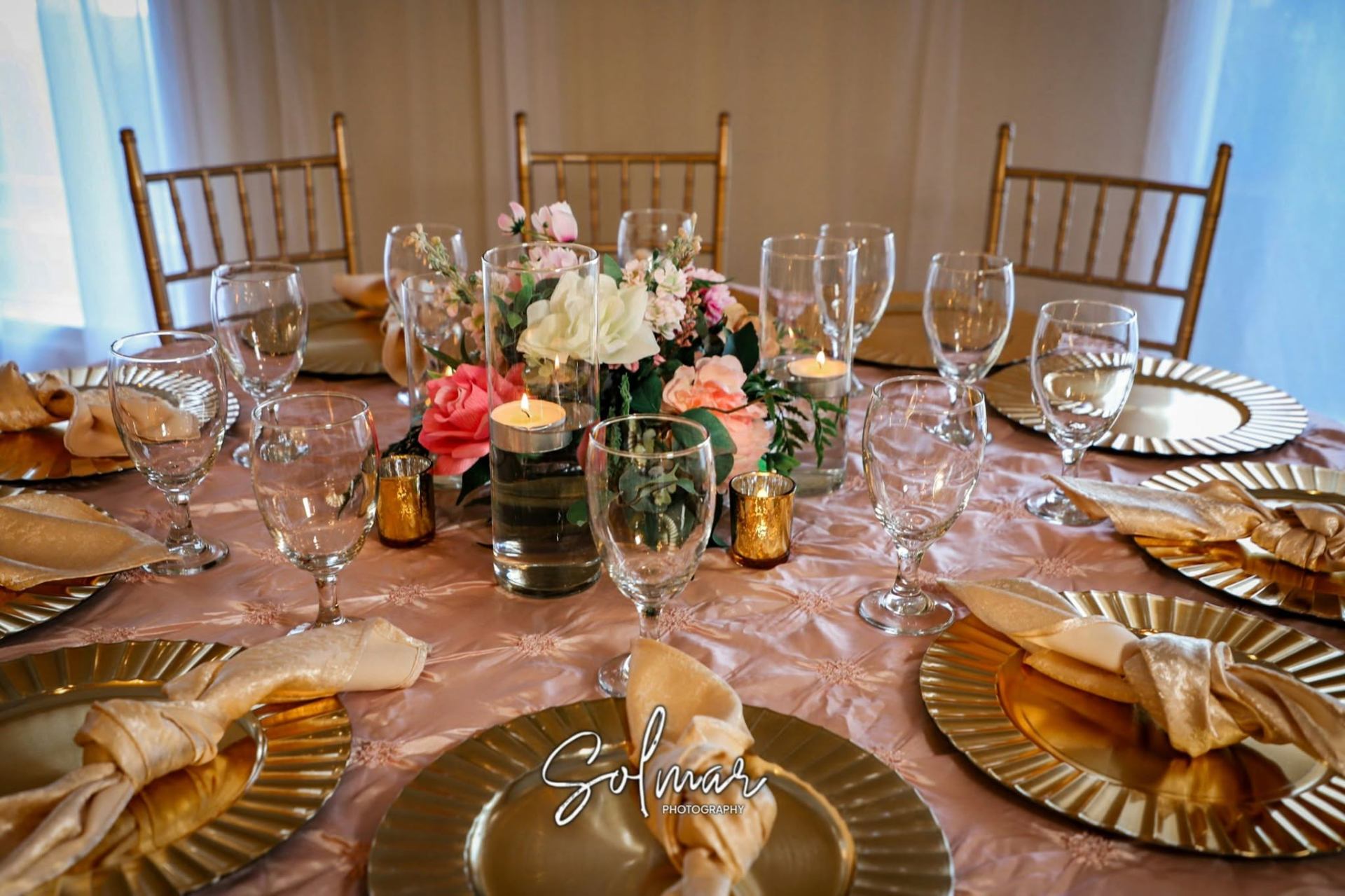 Close-up of gold chargers, satin napkins, and candles on a blush tablecloth
