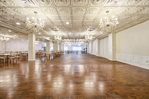 Grand venue open floor with chandeliers, ornate ceiling tiles, and gold chairs