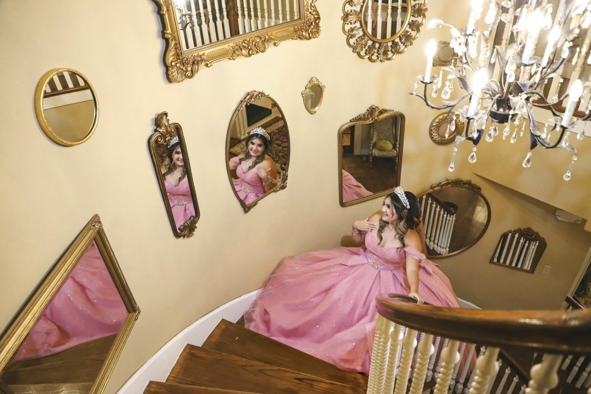 Quinceañera in a sparkling pink ballgown on the staircase beside gold-framed mirrors